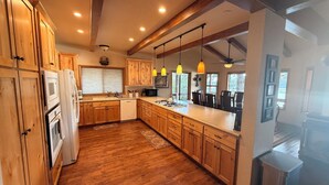 A modern kitchen with wooden cabinets, a central island, pendant lights, and a view of the outdoors. - Large 3-story LAKE VIEW 4 bedrooms (all masters) & 5 bath Boat Slip & Marina (Bass Lake)
