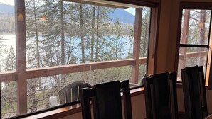 A room with a large window overlooking a forest and a lake. There are four wooden chairs and a table in the room. - Large 3-story LAKE VIEW 4 bedrooms (all masters) & 5 bath Boat Slip & Marina (Bass Lake)