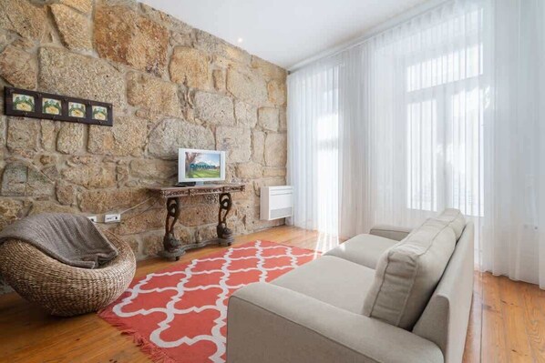 A living room with a stone wall, a sofa, a bean bag chair, a red patterned rug, and a picture frame.