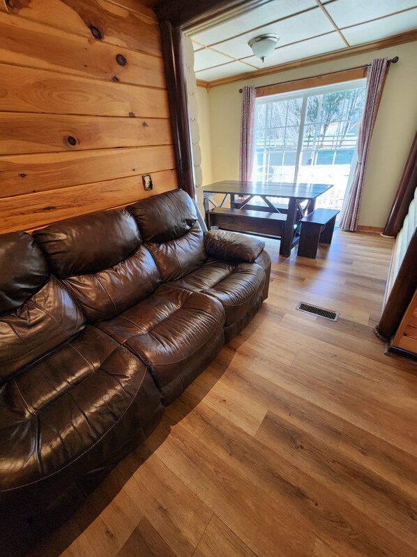 Una habitación con paneles de madera, un sofá de cuero, una mesa de comedor de madera y vistas a través de un ventanal grande.