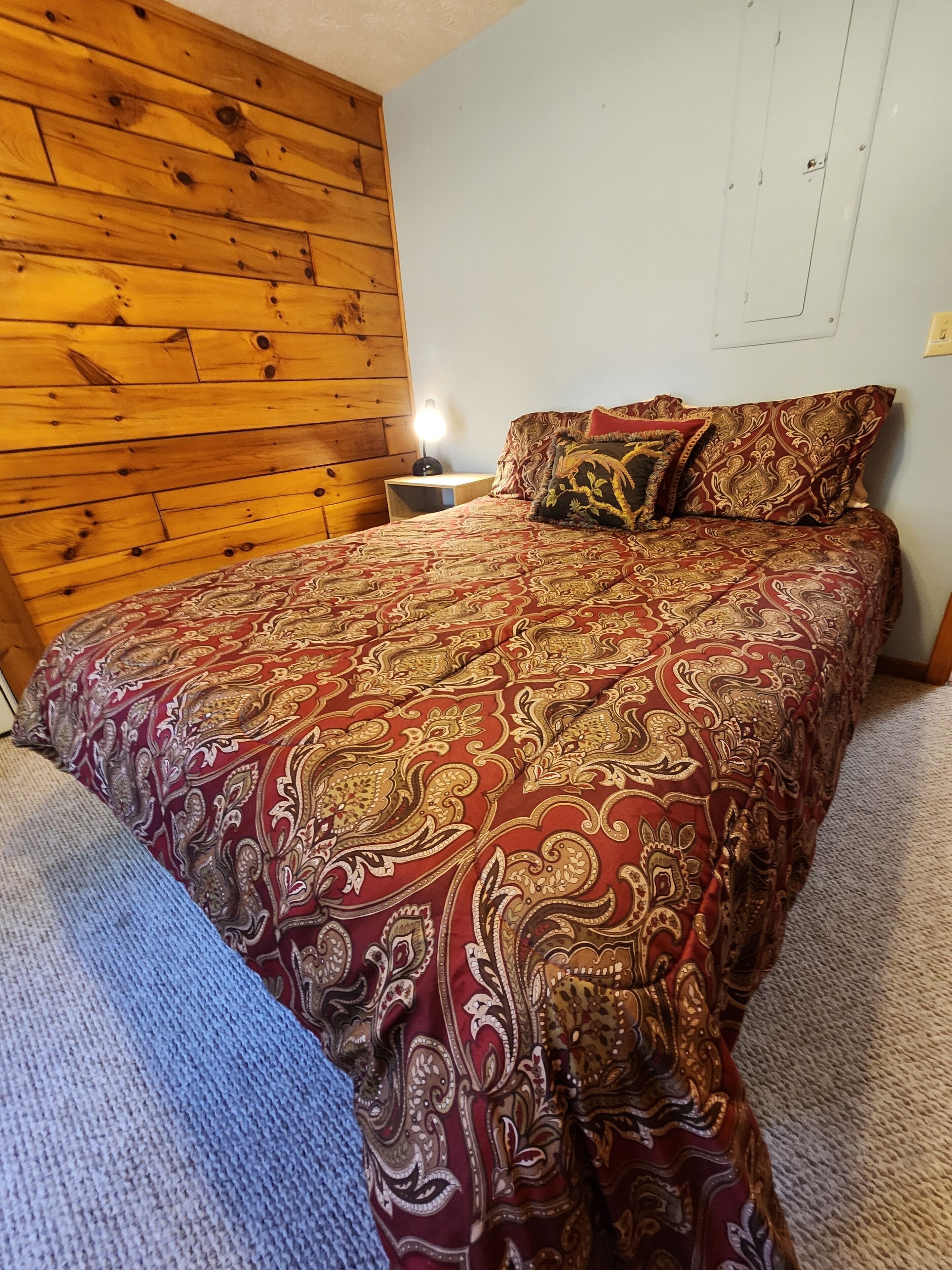Een slaapkamer met een houten hoofdeinde, een bed met een decoratieve spreidek en een bedlamp.