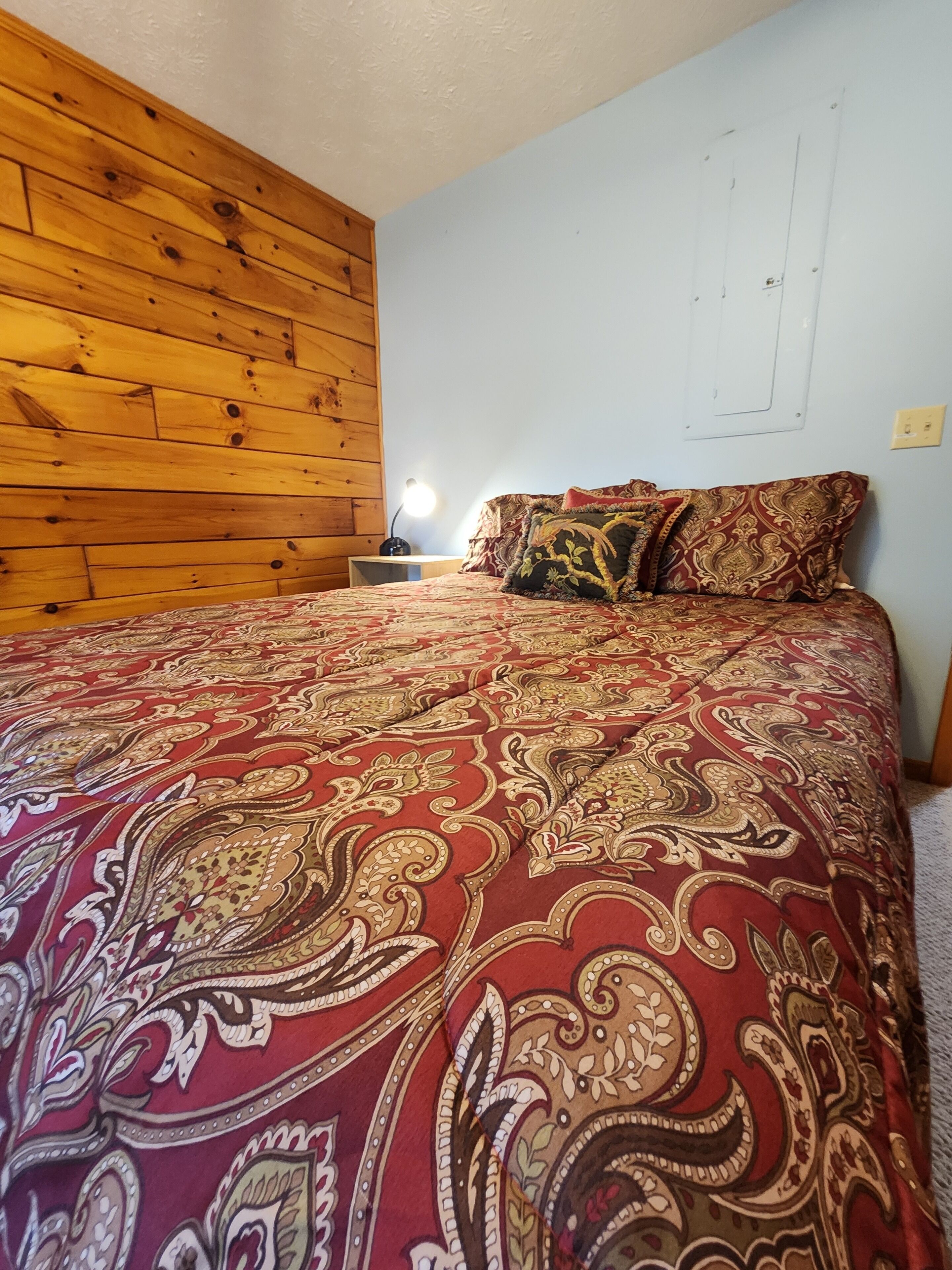 A bedroom with a wooden headboard, a patterned bedspread, and a bedside lamp.