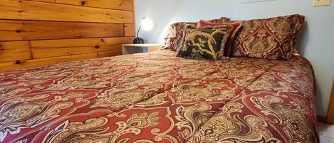 A bedroom with a wooden headboard, a patterned bedspread, and a bedside lamp.