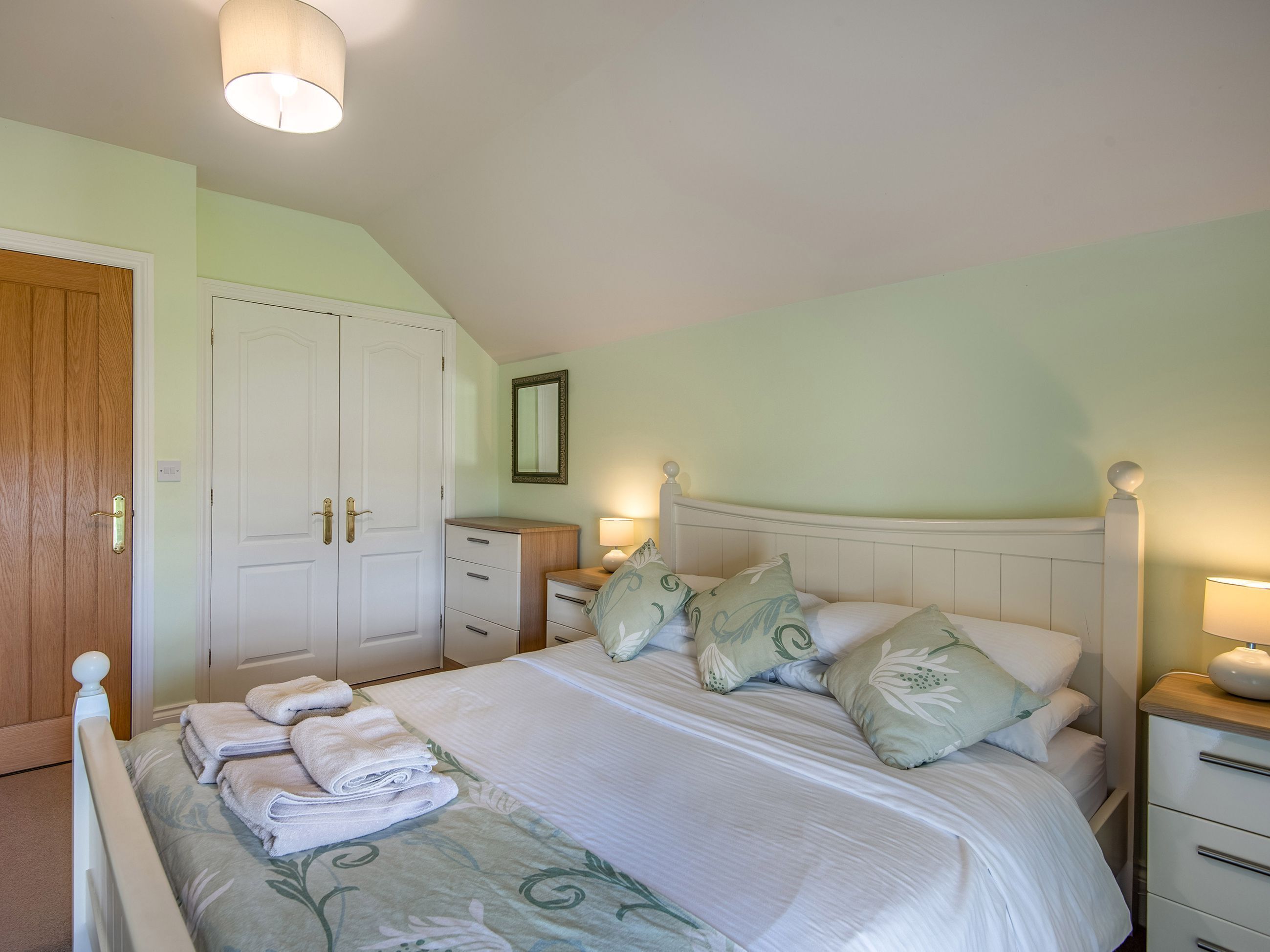 Une chambre à coucher comprenant un lit, des tables de chevet, une armoire et un miroir.