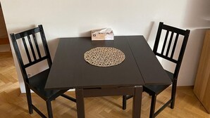 Ein dunkles Esstisch aus Holz mit einer gewebten Tischmatte, zwei schwarzen Stühlen und einer Papiertütenbox darauf.