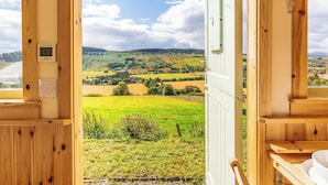 A wooden room with a view of green fields and hills. There is a thermostat and a light switch on the wall. - Woodside Hut 1 - UK36105 (Strathpeffer)
