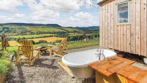A wooden cabin with a bathtub, two chairs, and a view of rolling hills. - Woodside Hut 1 - UK36105 (Strathpeffer)
