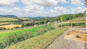 A scenic view of a countryside landscape with rolling hills, a clear sky, and a wooden deck with a bench. - Woodside Hut 1 - UK36105 (Strathpeffer)