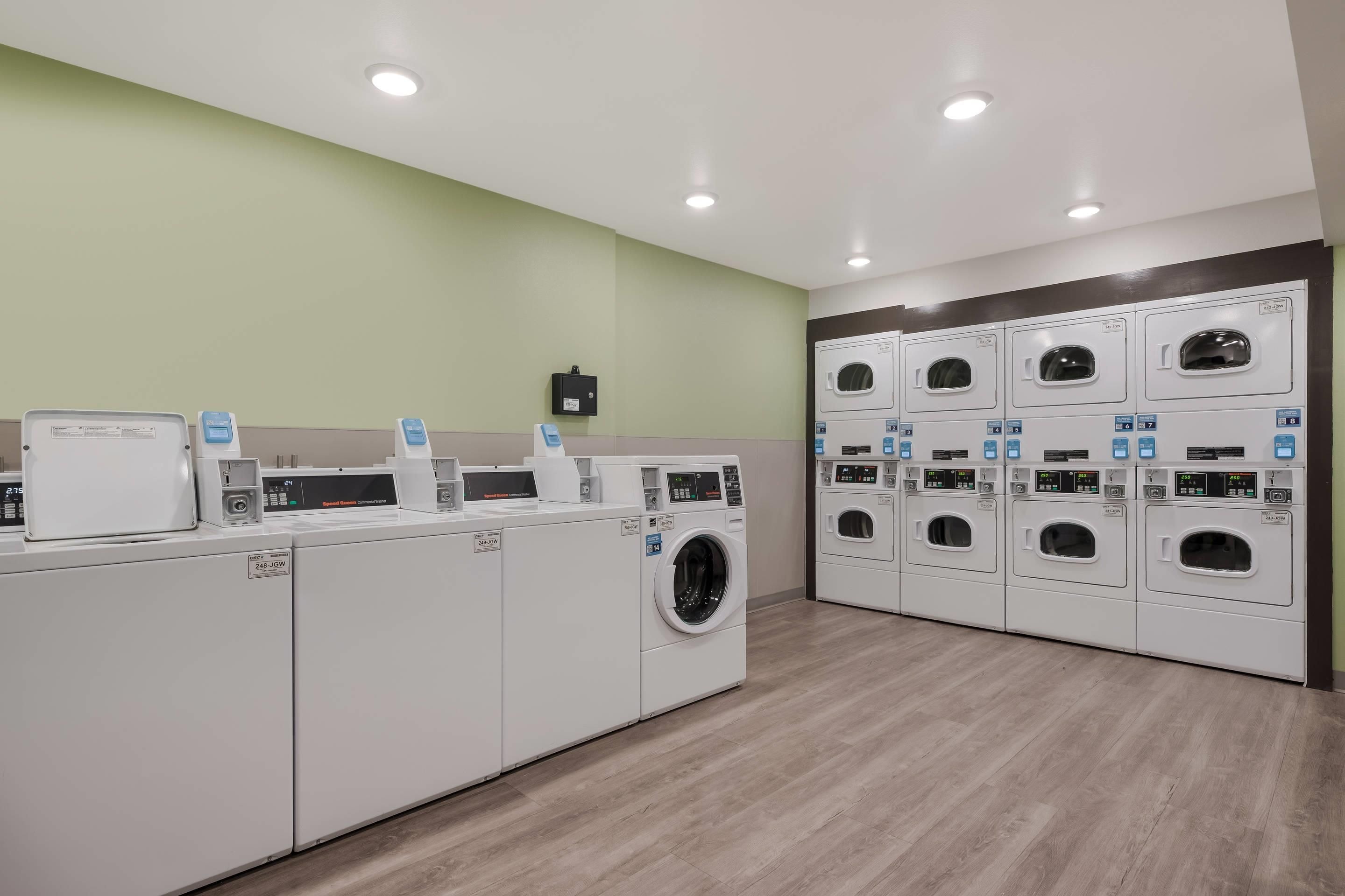 A laundry facility with multiple washing machines and dryers, a control panel, and a wall-mounted electrical box.