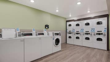 A laundry facility with multiple washing machines and dryers, a control panel, and a wall-mounted electrical box.