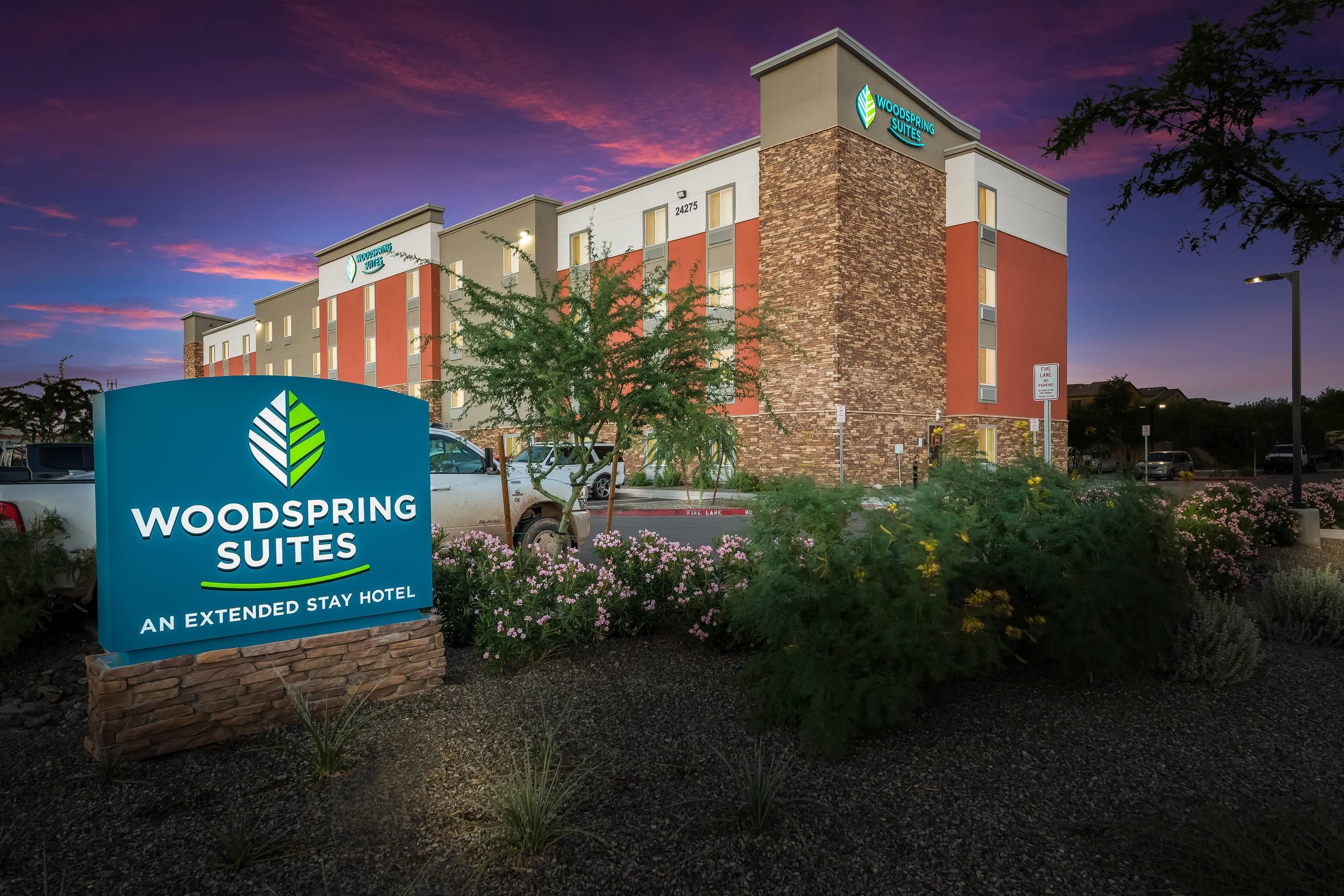 A hotel named Woodspring Suites with a signboard, a parking lot, and a building with a brick facade.