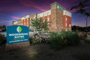 A hotel named Woodspring Suites with a signboard, a parking lot, and a building with a brick facade.