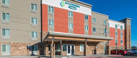 A two-story hotel with a modern facade, a prominent sign for Woodspring Suites, and a parking lot with marked spaces.