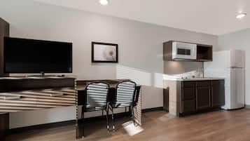 A modern kitchen with a microwave, refrigerator, and a dining area with a TV and chairs.
