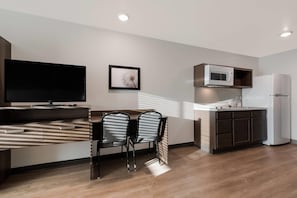 A modern kitchen with a microwave, refrigerator, and a dining area with a TV and chairs. - WoodSpring Suites Phoenix-Deer Valley (Phoenix)