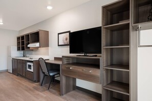 A modern kitchen with built-in appliances, a dining area with a chair, and a TV mounted on a wooden cabinet.