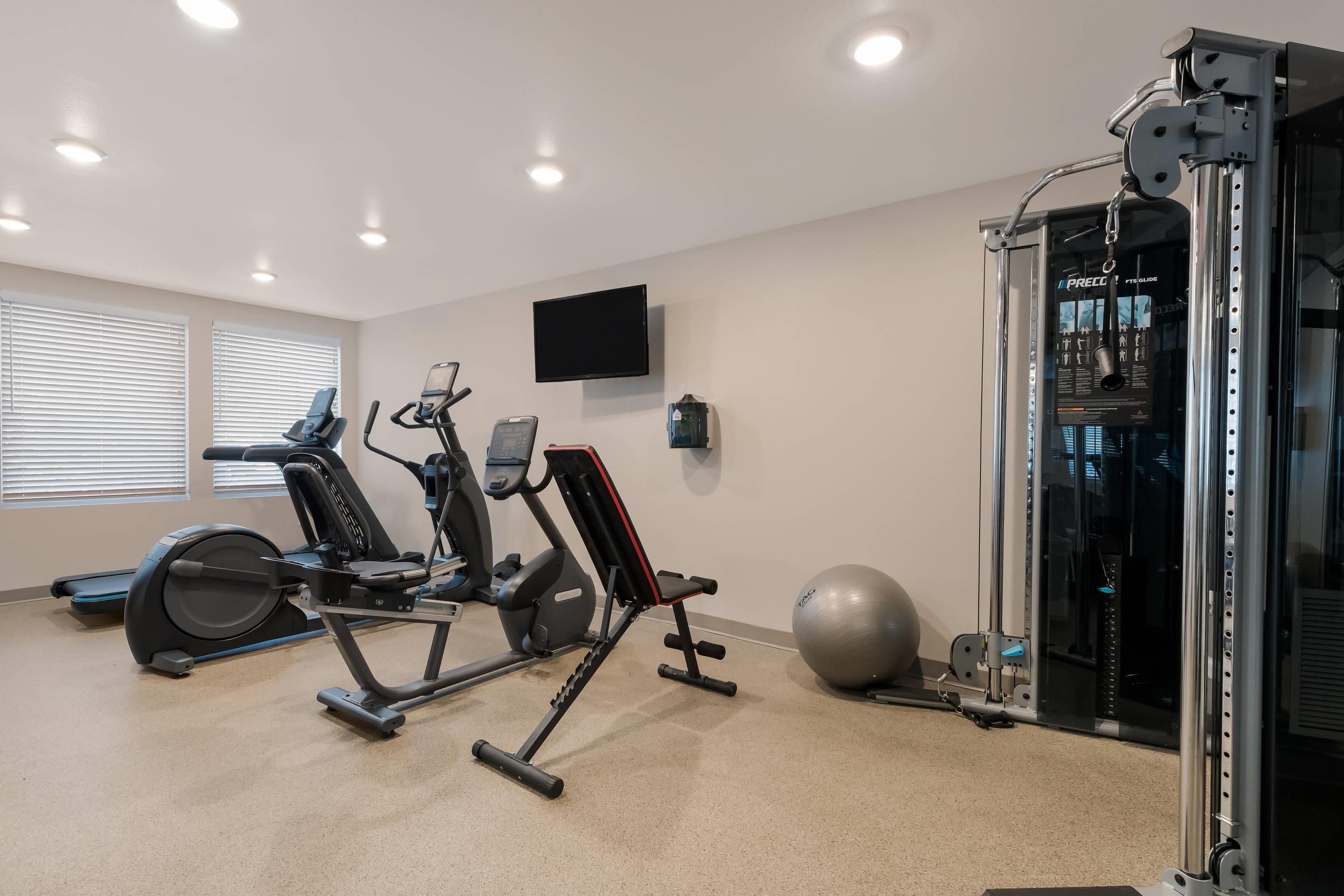 Een sportschool thuis met trainingsapparatuur, een televisie en een groot raam.