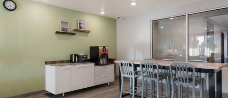 A modern kitchen with a coffee machine, a clock, and a dining area with chairs and a table.