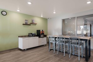 A modern kitchen with a coffee machine, a clock, and a dining area with chairs and a table. - WoodSpring Suites Phoenix-Deer Valley (Phoenix)
