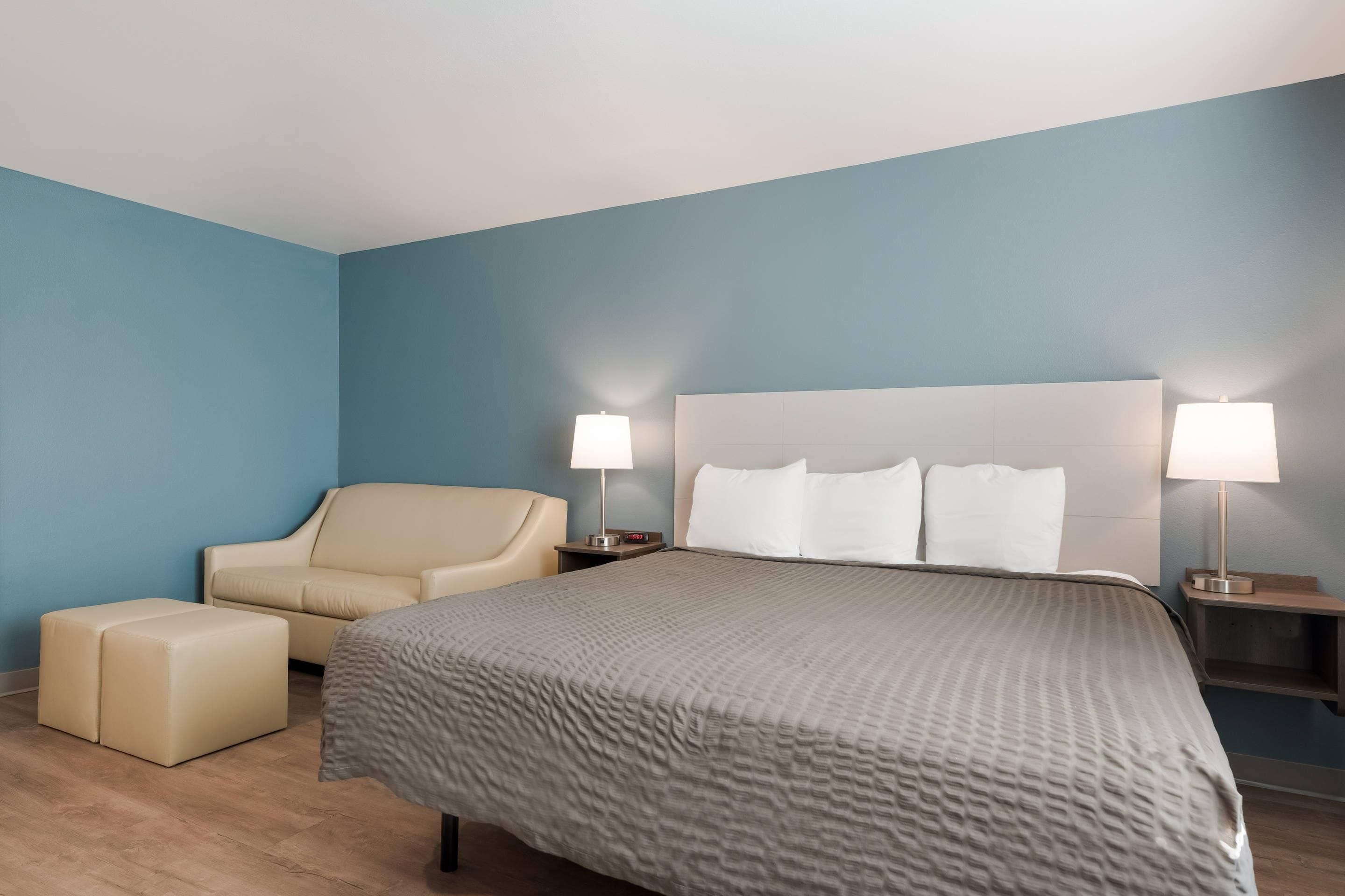 A hotel room with a bed, a chair, a nightstand, and a lamp.