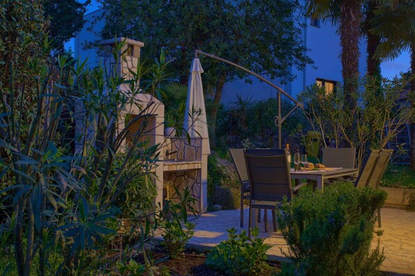 Une terrasse extérieure avec un barbecue en pierre, une table à manger, des chaises et un parasol incurvé.