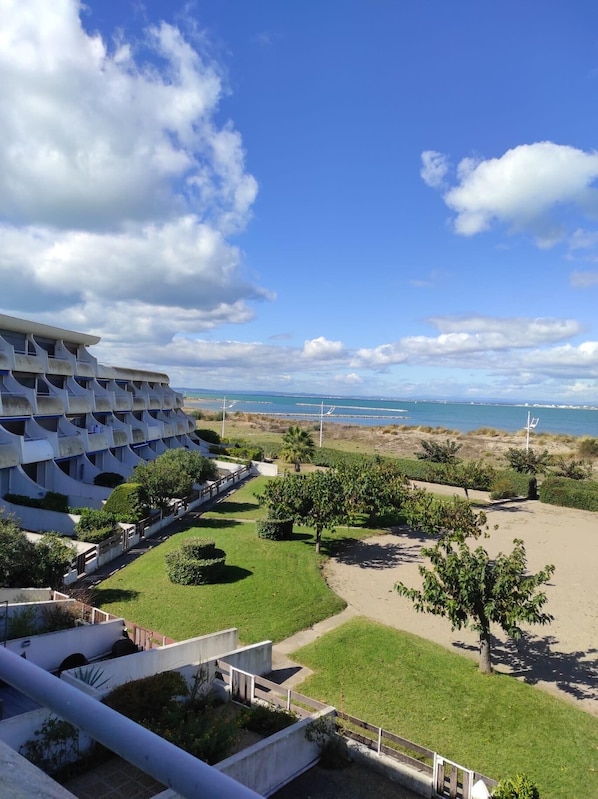 A hotel with a unique architectural design featuring multiple balconies. The property includes landscaped areas with trees and a view of the sea.