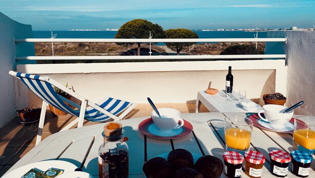 En terrasse med et bord dækket til morgenmad, med udsigt over kysten.