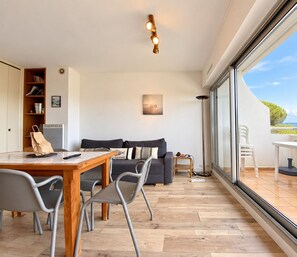 A modern living room with a dining area, a sofa, a table, and a view through large windows.