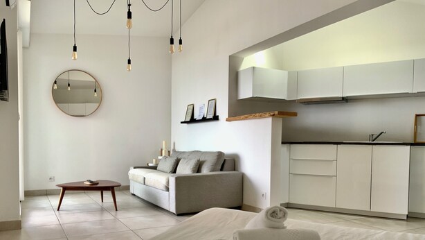 Un dormitorio moderno con cama, sofá, espejo redondo y zona de cocina.