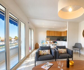A modern living room with a large window, a dining area, and a kitchen.