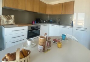 A modern kitchen with wooden cabinets, a white countertop, and various breakfast items including bread, cereal, and juice.