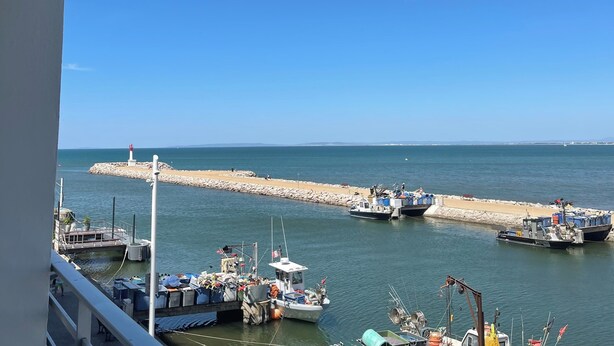 Un port de plaisance avec des bateaux amarrés, un phare et une digue rocheuse.