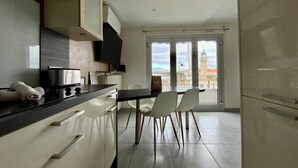 Une cuisine moderne avec un coin repas, dotée d’une grande fenêtre offrant une vue sur un phare et la mer.