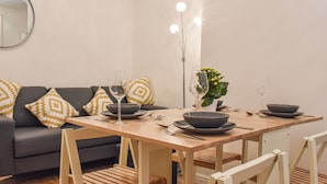 A dining area with a wooden table set for two, accompanied by a grey sofa with patterned cushions.