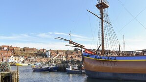 A large sailing ship docked at a harbor with a town in the background.