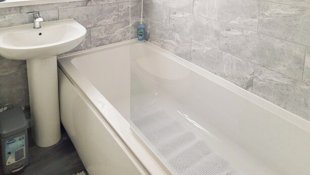 A bathroom with a white bathtub, a pedestal sink, and a window with a view of the outside.