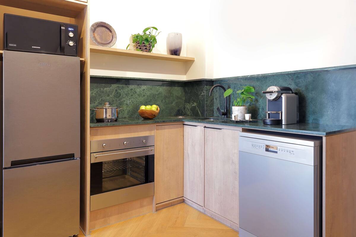A compact kitchen with a refrigerator, oven, dishwasher, and a coffee maker on the countertop.