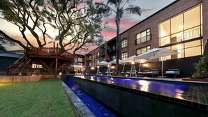 A swimming pool with a wooden deck and lounge chairs, surrounded by a brick building with large windows and a tree. - Hyatt House Johannesburg, Sandton (Sandton)