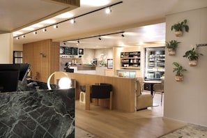 A modern hotel lobby with a reception desk, seating area, and a kitchen in the background.