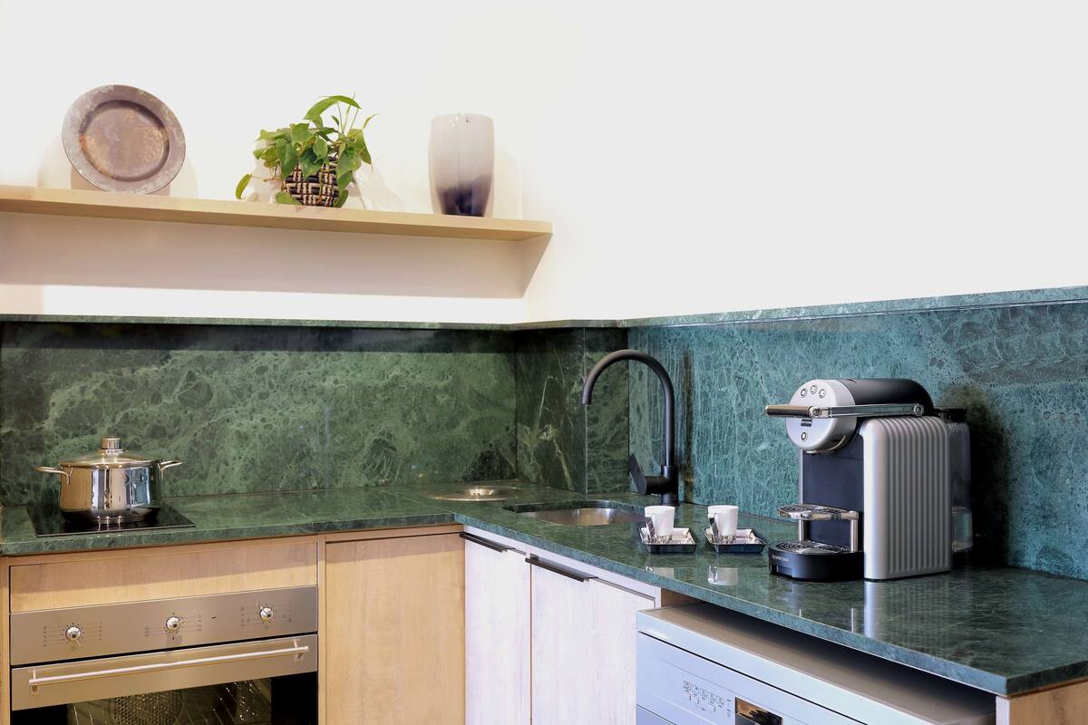 A kitchen with a green marble countertop, a coffee machine, a sink, and a dish rack.