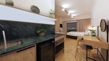 A compact hotel room with a kitchen area, a bed, a desk, and a view of the cityscape.