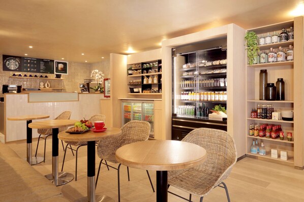 A modern cafe with wicker chairs, a coffee bar, and shelves stocked with condiments and beverages.