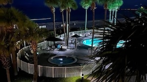 Un espace piscine d’un complexe hôtelier, aménagé pour la nuit, avec un jacuzzi circulaire, des palmiers et une vue sur l’océan.
