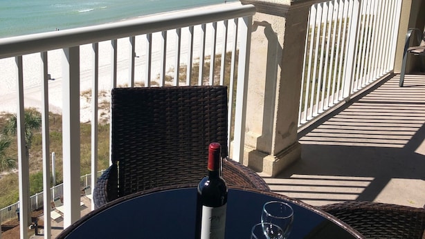 Un balcon avec une table, une bouteille de vin et deux verres. En arrière-plan, une jetée s’avance dans l’océan.