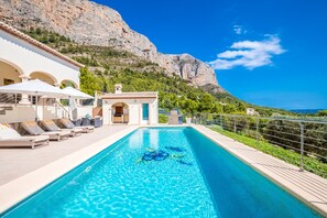 A swimming pool with lounge chairs and umbrellas, a mountain backdrop, and a clear sky. - 4 Bedroom Villa with Spectacular Views (Jávea)