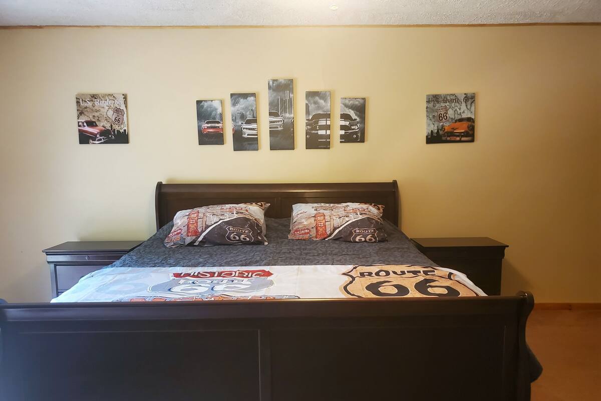 Een bed met een sprei in Route 66-thema, twee kussens, een nachtkastje en een muur met vier schilderijen in Route 66-thema.