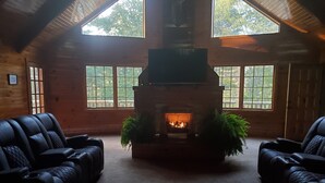 Una habitación acogedora con chimenea, sillones de cuero y ventanas grandes.