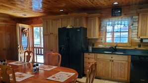 Interior de una cabaña de madera con una mesa de comedor, sillas, un refrigerador negro, armarios de madera, una ventana con vistas y un lavabo.