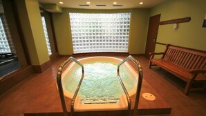 Een spa ruimte met een jacuzzi, houten banken en een raam met een decoratieve blind.