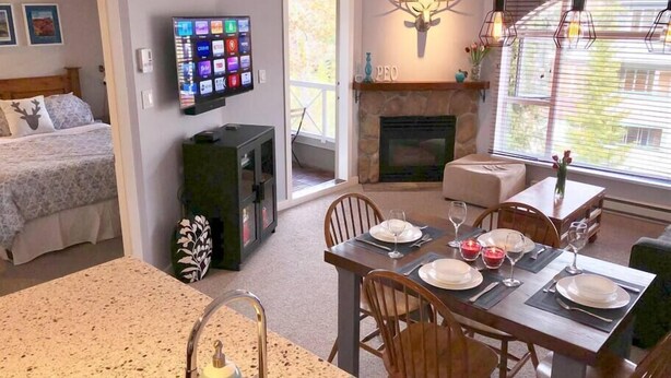 Een gezellige kamer met een bed, een eethoek met een tafel gedekt voor twee personen, een open haard en een aan de muur bevestigde televisie.